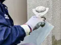 Murarz nakłada tynk elewacyjny na ścianę za pomocą kielni.