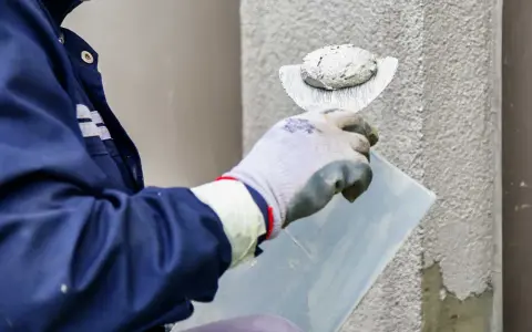 Murarz nakłada tynk elewacyjny na ścianę za pomocą kielni.