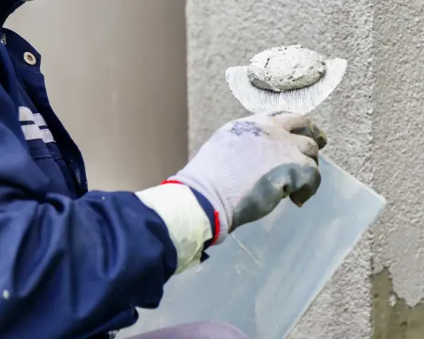 Murarz nakłada tynk elewacyjny na ścianę za pomocą kielni.